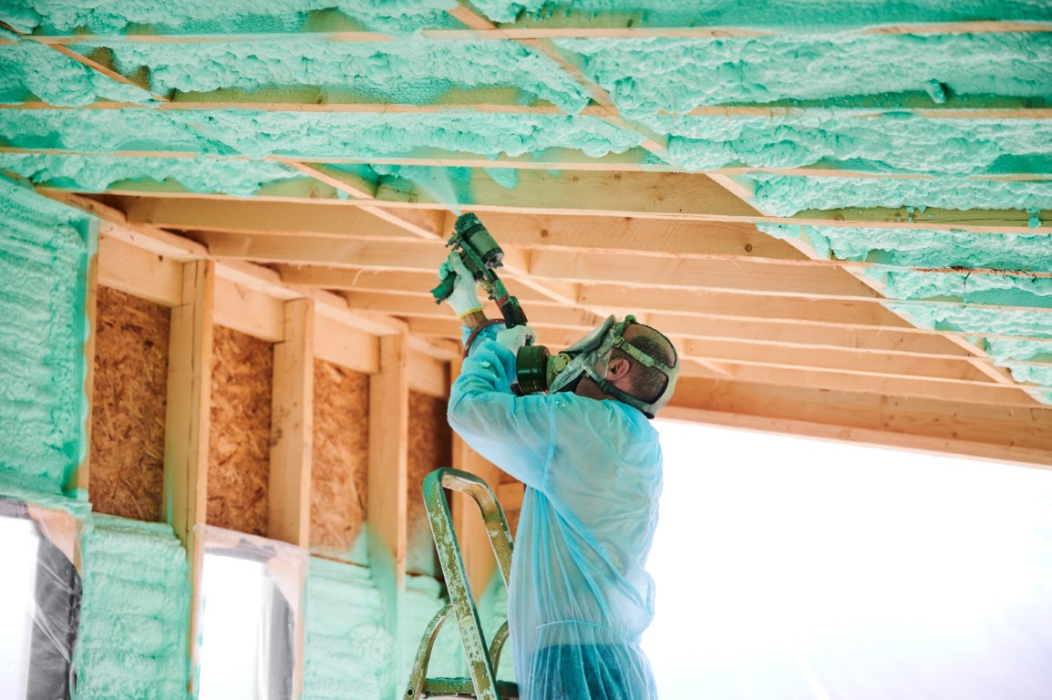 A picture of a man performing a foam insulation on a celling of an establishment.
